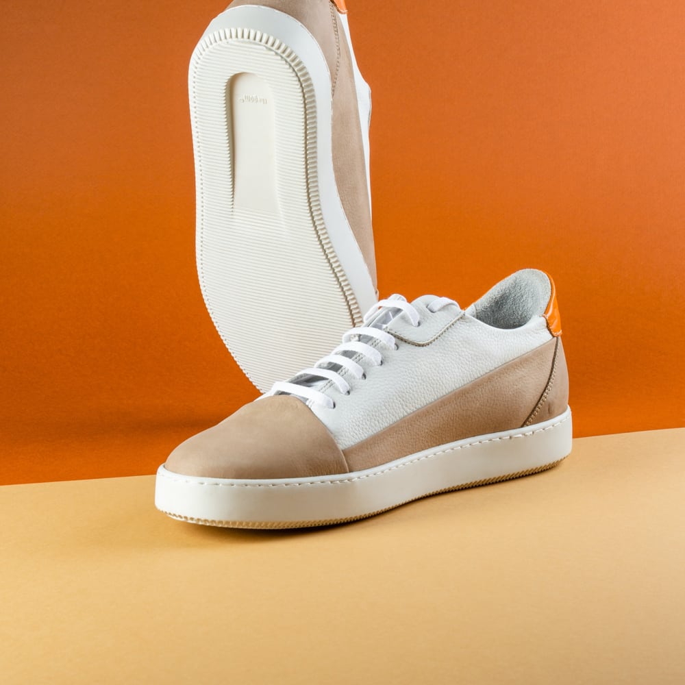 Shoes with a white sole, tan toe cap, a white upper portion with white  laces, and an orange patch on the heels.